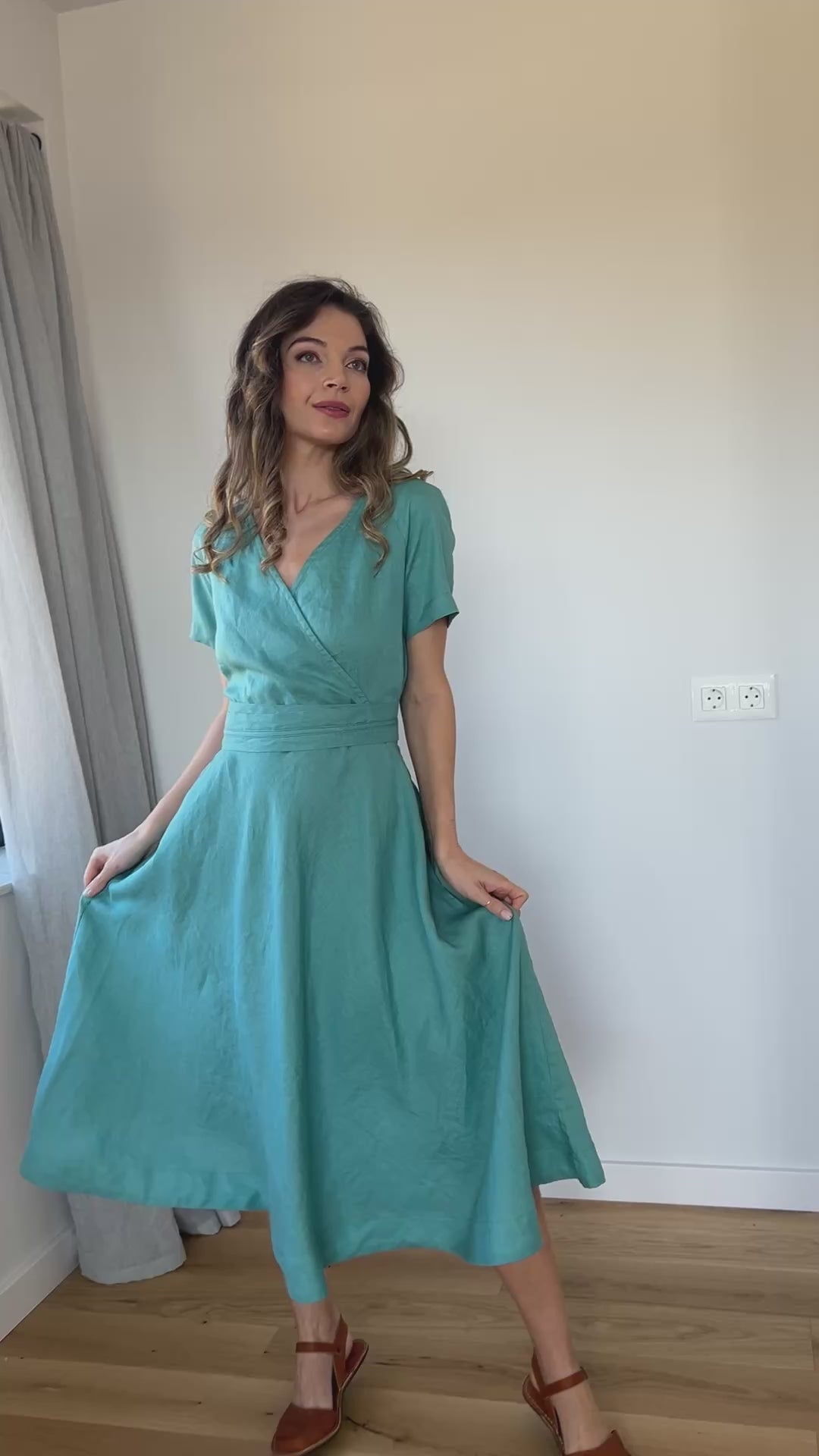 Video of a linen midi faux wrap dress with a surplice neckline, elastic waist, matching obi belt, and side pockets, showing the fit and movement of the design.