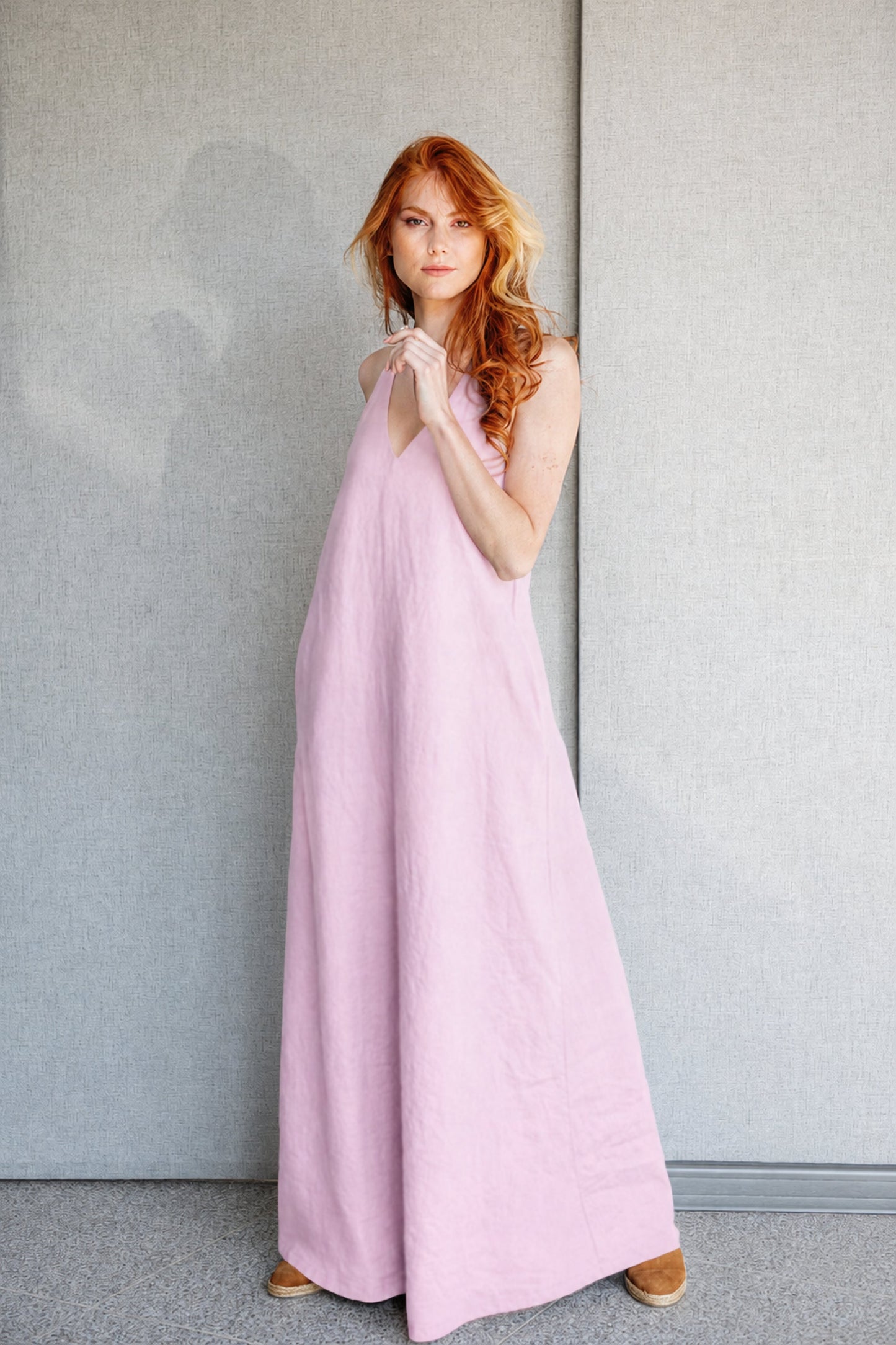 Minimalist linen sleeveless dress in pink with deep V-neck and halter back, worn by model.