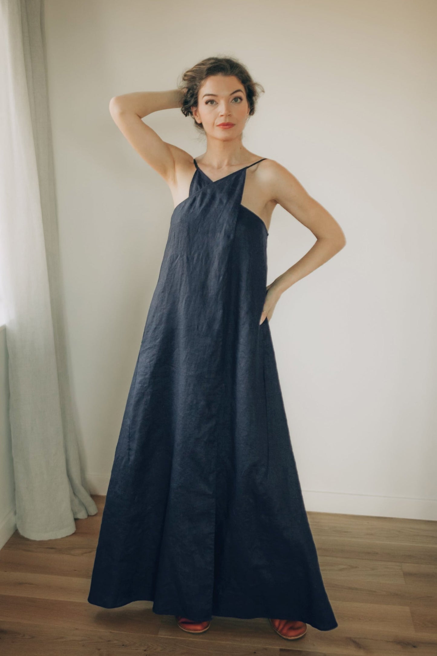 Woman wearing a navy blue linen dress in a room with wooden flooring and a window.