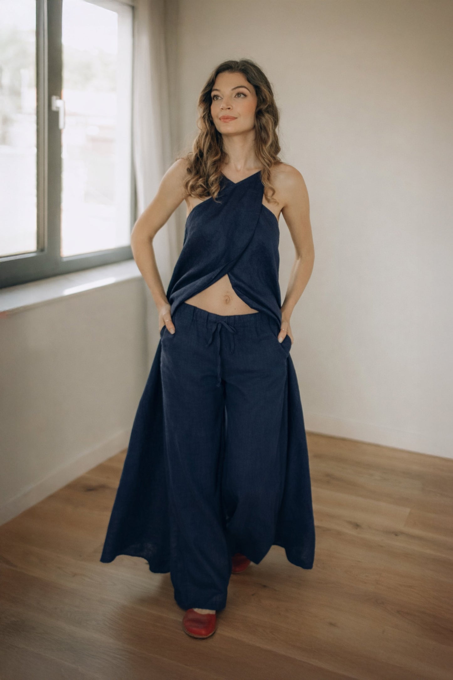 Woman wearing a navy blue linen dress with pants standing in a room with wooden flooring and a window.