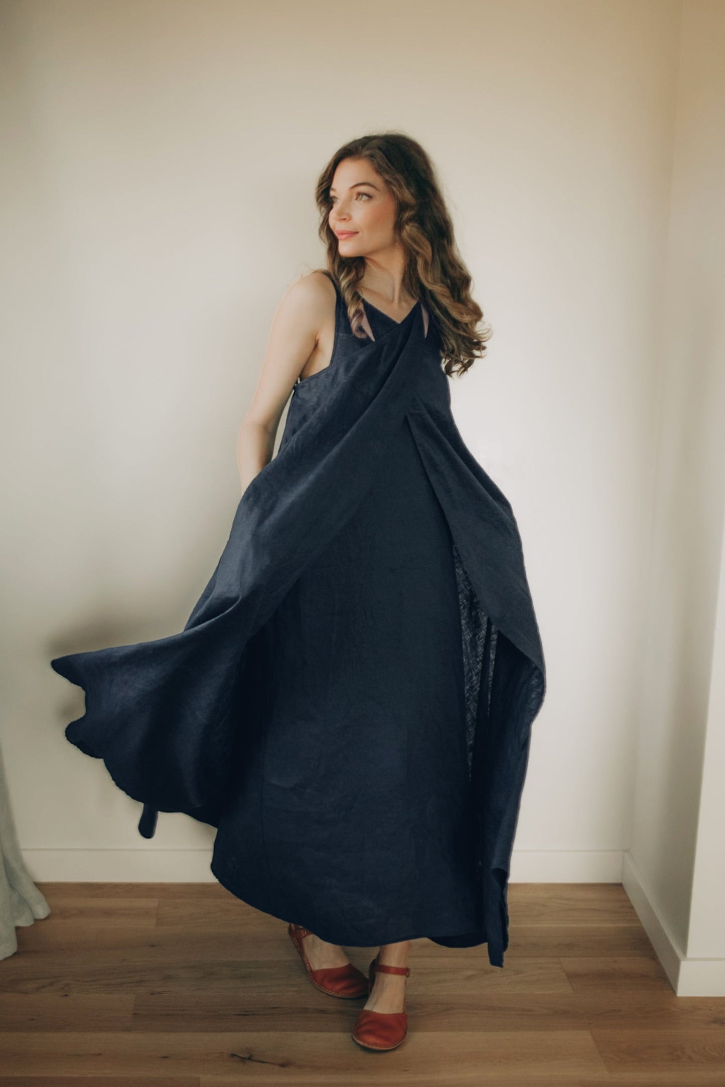 Woman wearing a navy blue linen  dress standing in a room with wooden floor and white walls.