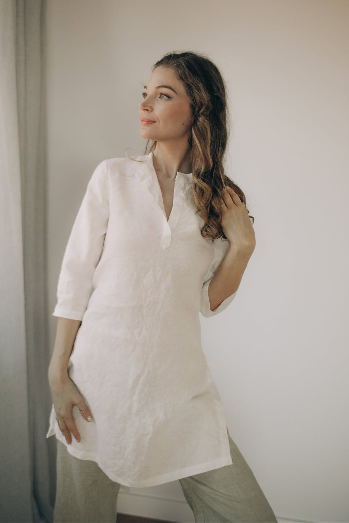 White minimalist linen tunic top with kaftan cut, split shirt neckline, and three-quarter sleeves on model