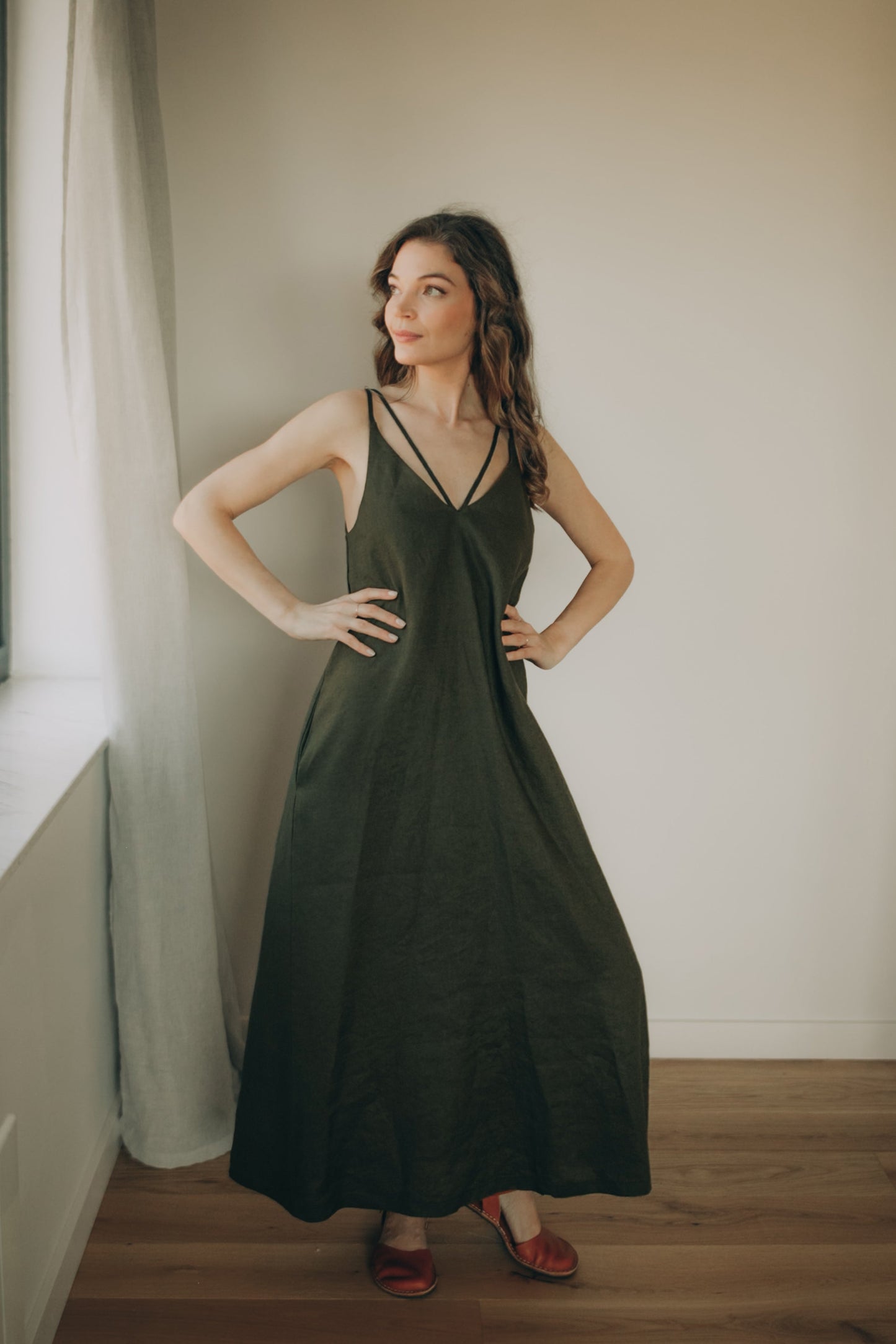 Woman wearing a green linen dress standing in a room with a neutral background