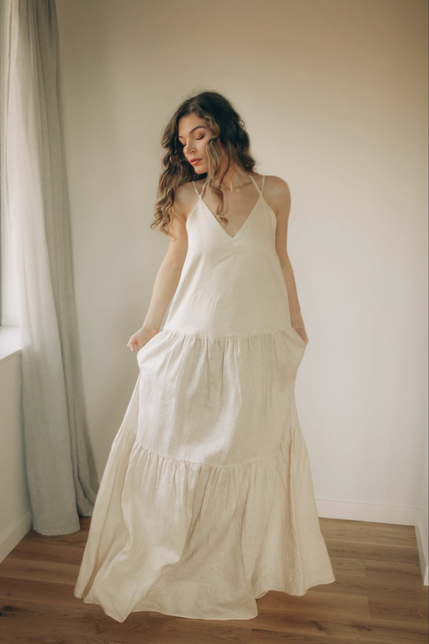Cream tiered linen maxi dress with pockets, adjustable straps, and flowing silhouette