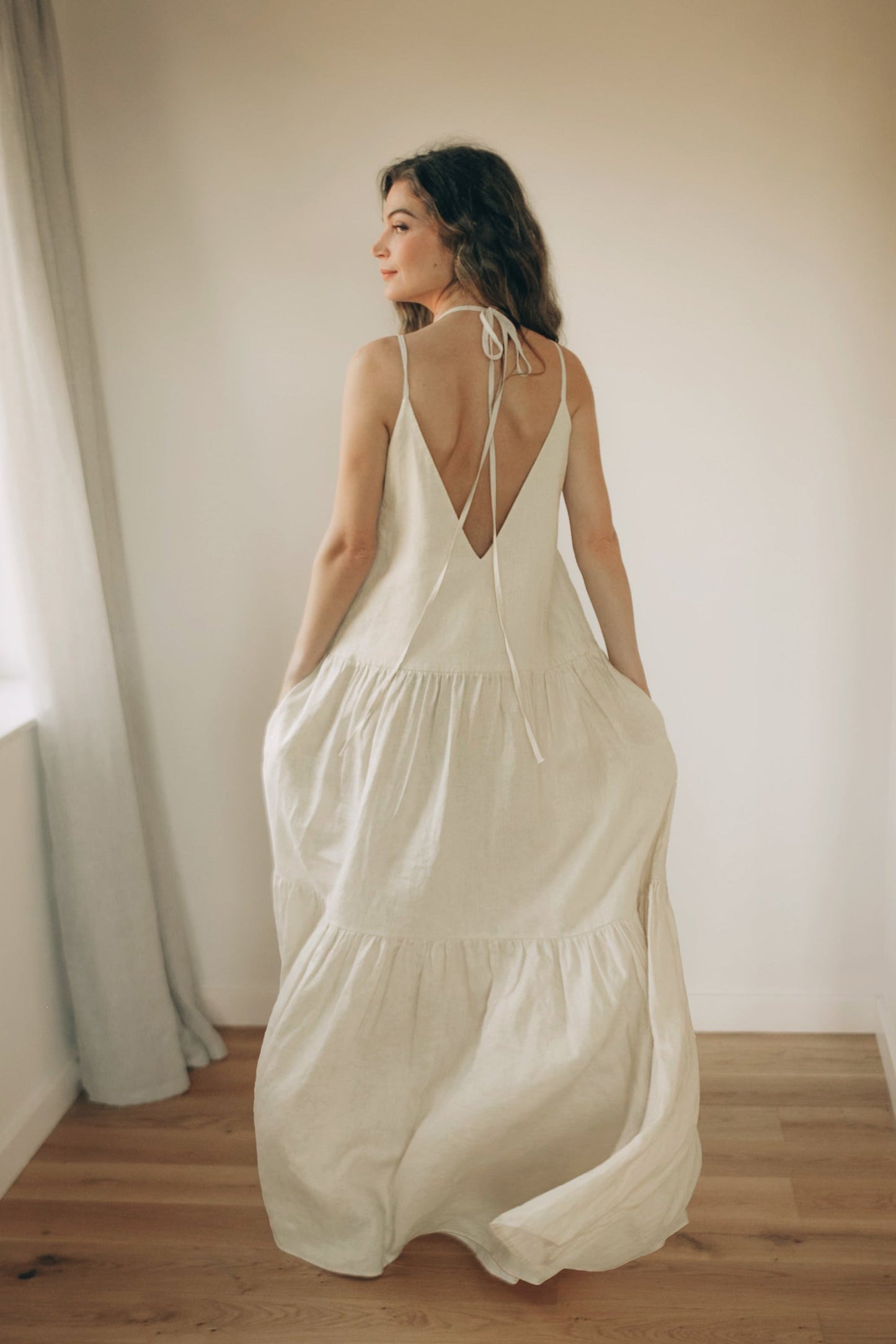 Cream tiered linen maxi dress with pockets, adjustable straps, and flowing silhouette