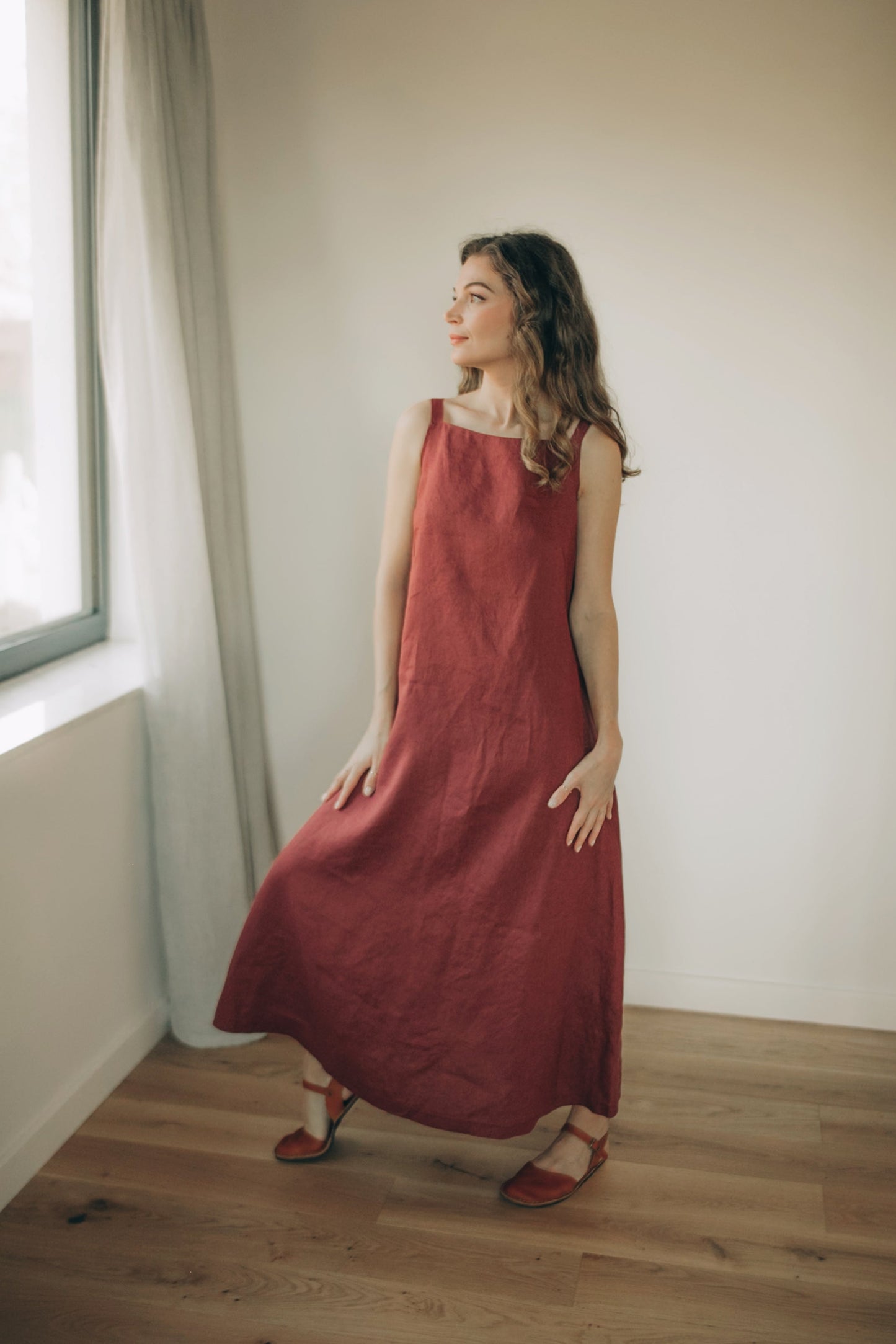 Woman wearing minimalist linen A-Line midi dress with shoulder straps and side pockets