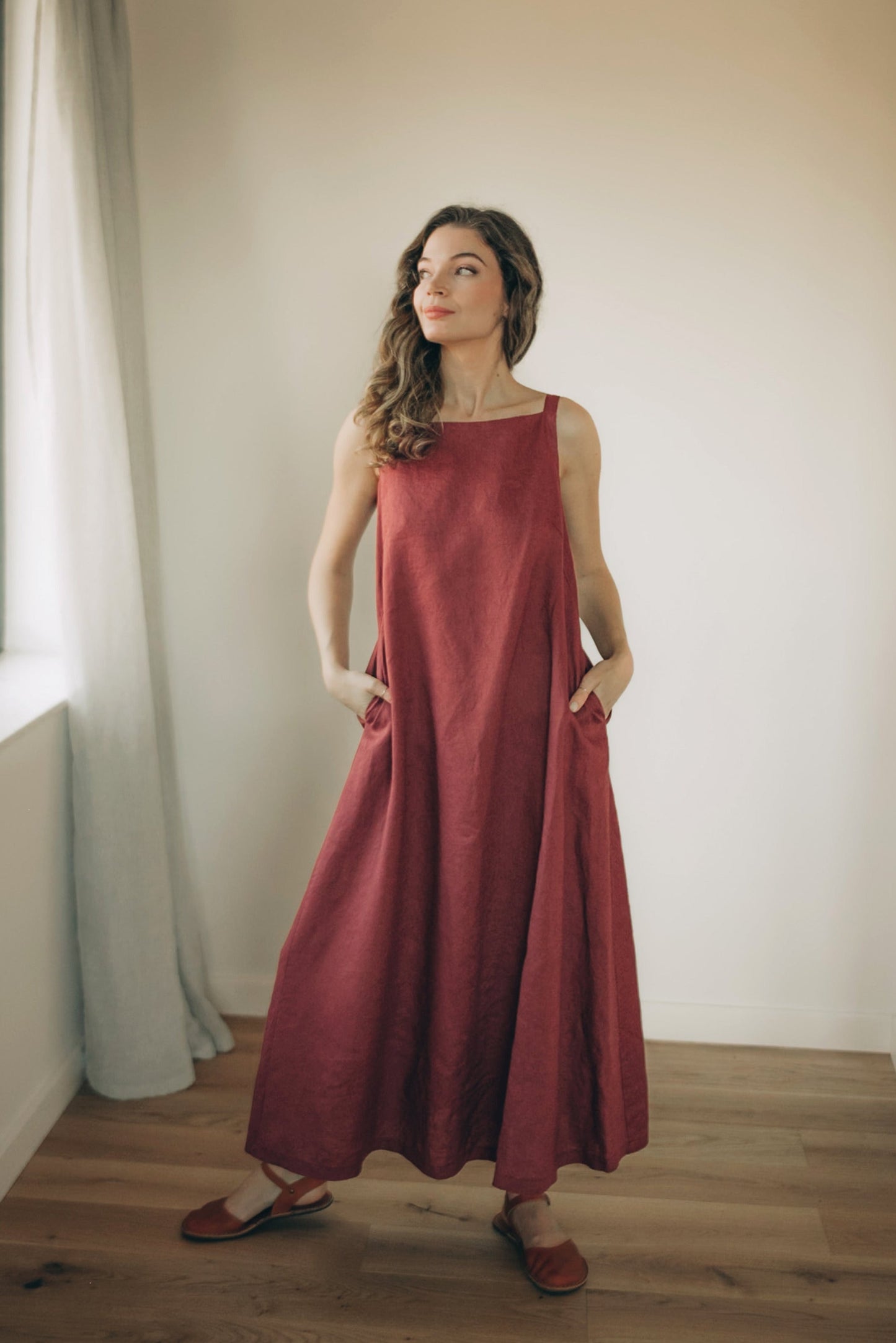 Woman wearing minimalist linen A-Line midi dress with shoulder straps and side pockets